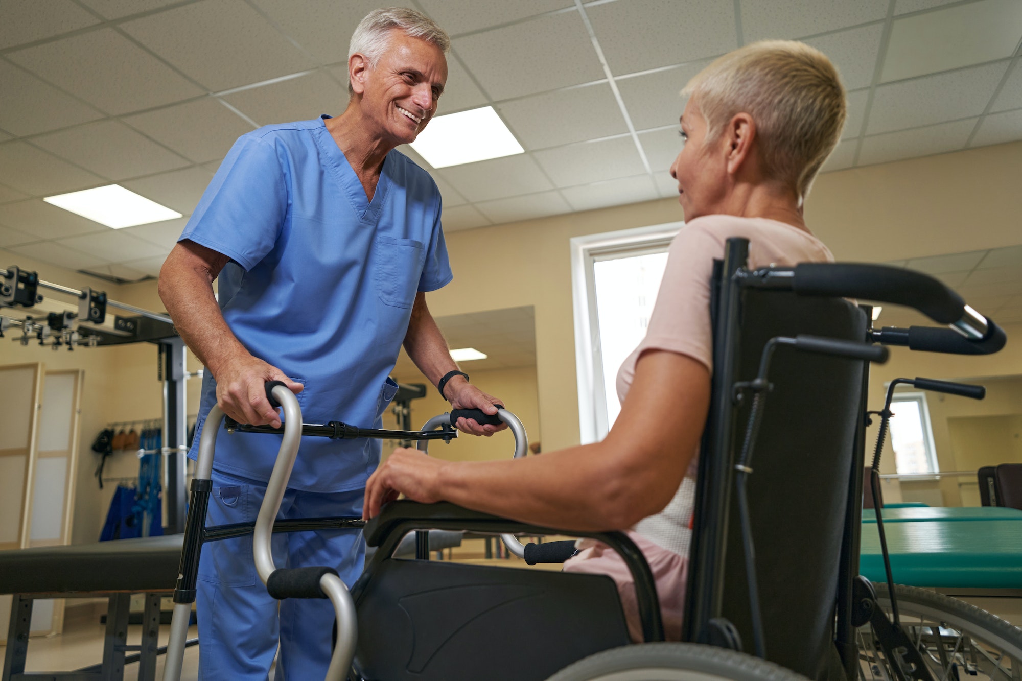 Healthcare professional helping mature woman to use walker in clinic