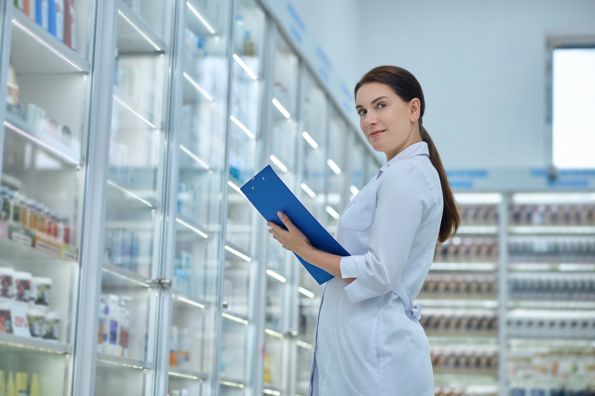 Pharmacist posing for the camera among shelves with healthcare products