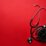 Stethoscope and alarm clock on red background. Medical and health care concept.
