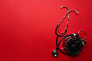 Stethoscope and alarm clock on red background. Medical and health care concept.